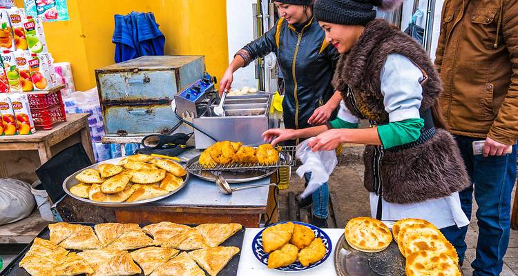 Vendedores del mercado friendo pasteles y panes dorados en un puesto colorido de comida callejera.