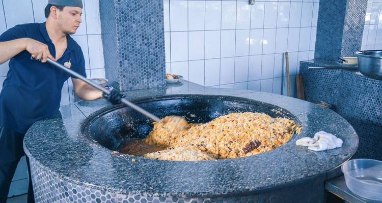 Cuisinier remuant un énorme chaudron de plov dans une cuisine ouzbèke carrelée