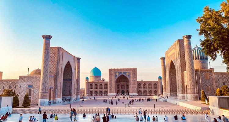 La majestueuse place du Régistan avec ses madrasas monumentales illuminées par la lumière chaude du soir et les foules en bas