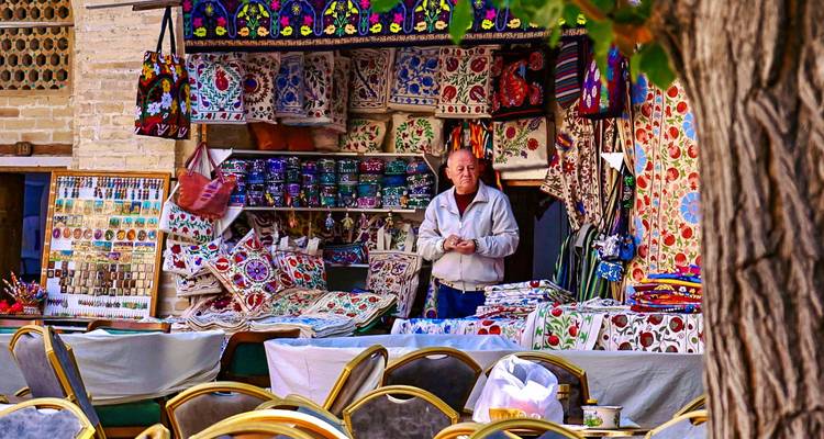 Vendeur à l'étal de textiles colorés du bazar de Boukhara entouré de tissus brodés