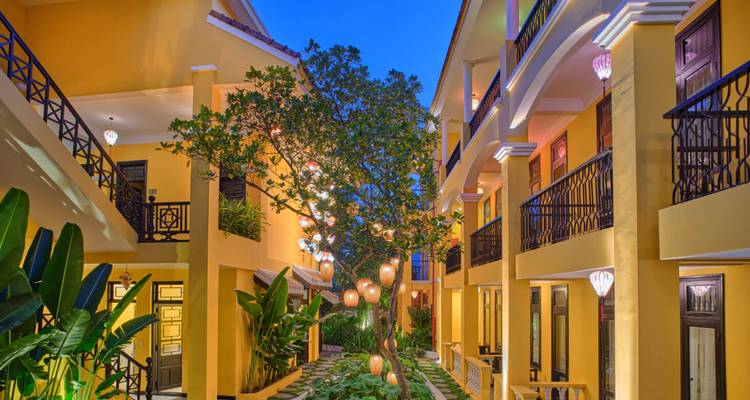 Un patio al atardecer iluminado por faroles de colores colgados de un árbol central en un hotel boutique.