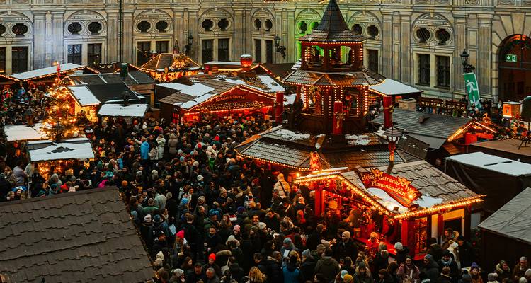 Crowded illuminated Christmas market stalls filling a historic courtyard at dusk