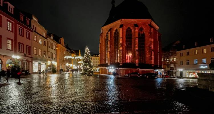 Rain-slicked cobblestone square at night with softly lit historic church and Christmas decorations