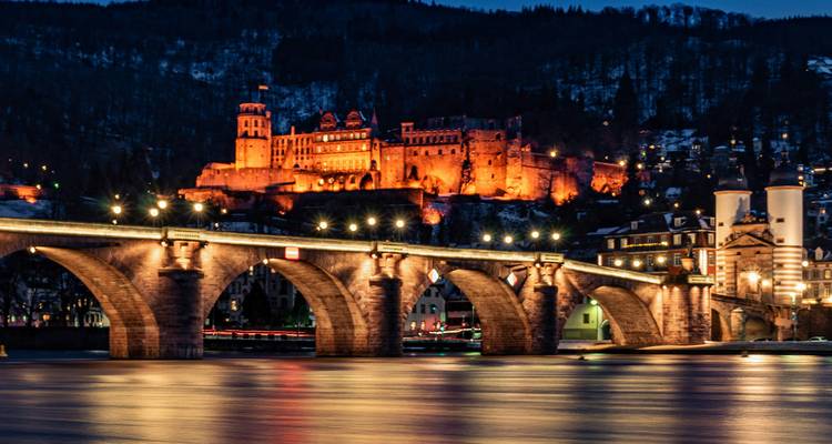 Heidelberg Castle glowing above the illuminated Old Bridge reflected in the Neckar River at night