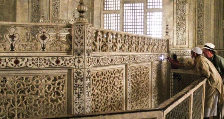 Visitantes observando intrincados trabajos de celosía de mármol dentro del mausoleo del Taj Mahal