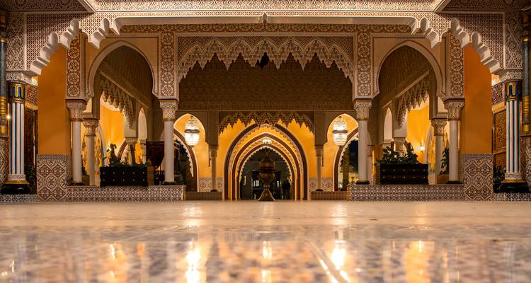 Lavishly decorated interior hall with Moorish arches, tilework and warm lighting.