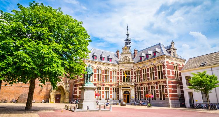 Salle historique de l'Université d'Utrecht dans une cour ensoleillée encadrée par un arbre feuillu et des vélos.