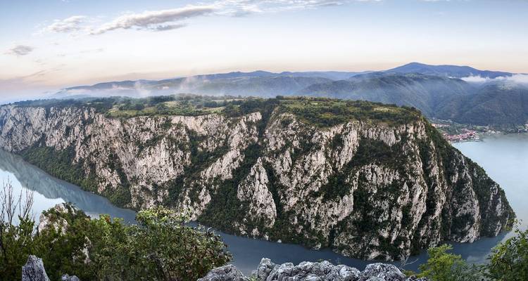 Dramatic aerial panorama of the Danube slicing through limestone cliffs of the Iron Gates gorge at dawn.