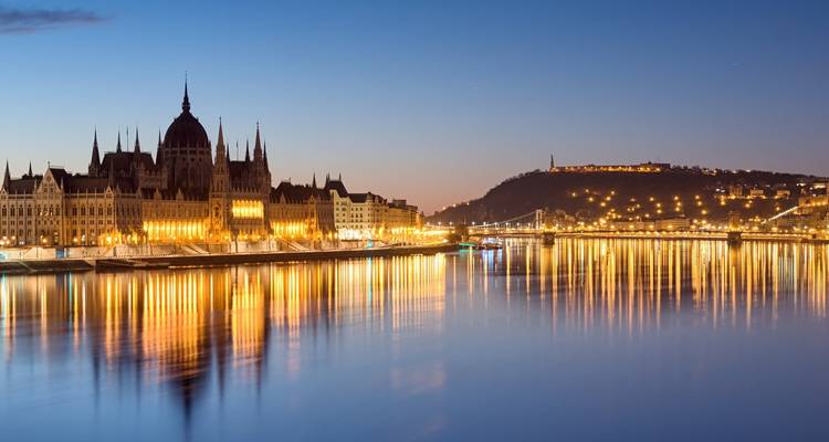 Le Parlement hongrois illuminé and les collines de Buda se reflètent sur le Danube calme au crépuscule.