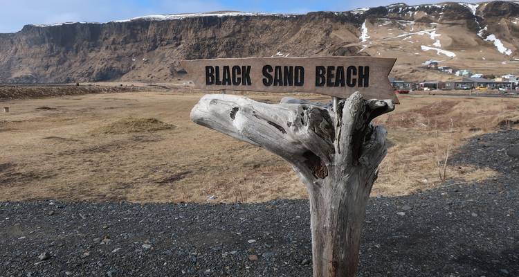 Ein rustikales Holzschild weist den Weg zum Schwarzen Sandstrand in Island.