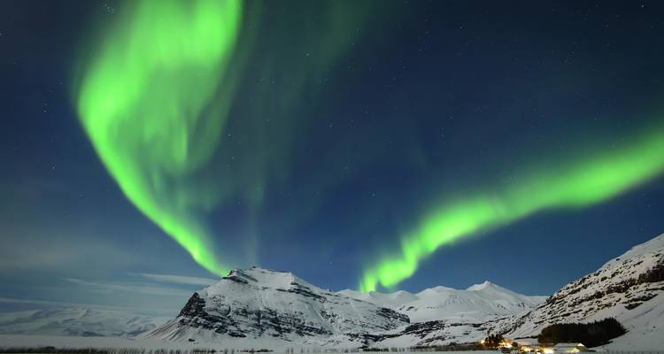Leuchtend grüne Nordlichter tanzen über schneebedeckte Gipfel in einer klaren Nacht.