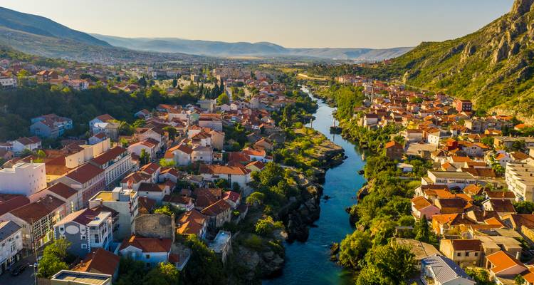 Luchtfoto van huizen met rode daken en smaragdgroene rivier die zich door een Balkanbergdal slingert