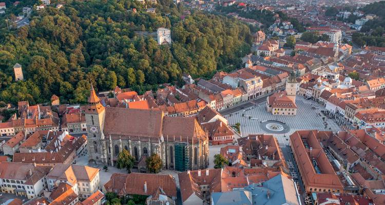 Luchtfoto bij zonsondergang van het historische centrum van Brașov, de Zwarte Kerk en omringende beboste heuvel