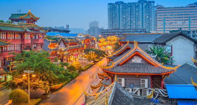 Edificios tradicionales de madera roja y faroles bordean una calle animada en Chengdu al atardecer.