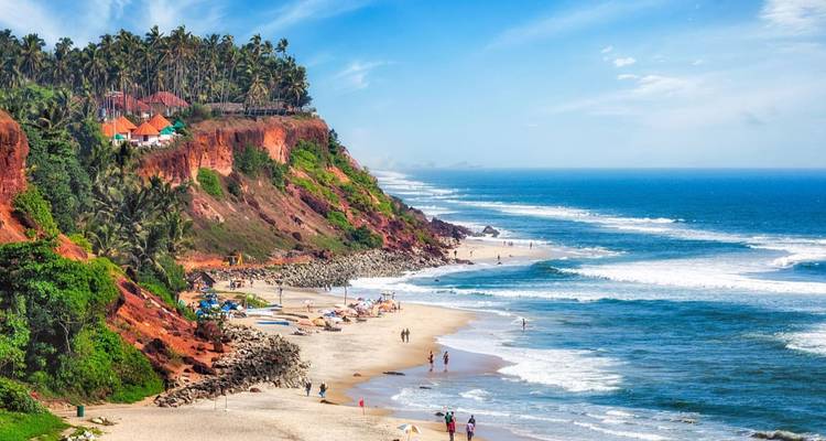 Rode laterietrotsen met palmbomen erop die uitkijken over een lang zandstrand en rollende golven.
