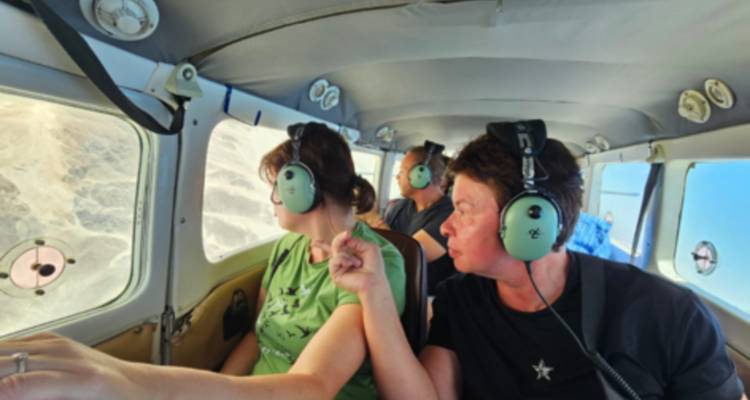 Toma interior borrosa de turistas usando auriculares mirando por la ventana de un avión pequeño hacia el terreno desértico.