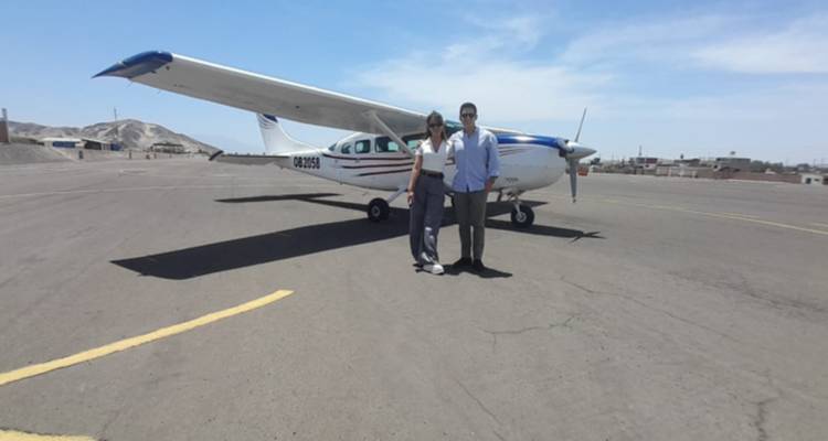 Imagen borrosa de dos viajeros de pie junto a un avión pequeño en una pista de aterrizaje del desierto.