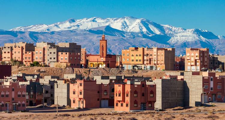 Moderna ciudad de estilo adobe de Ouarzazate con las montañas nevadas del Atlas elevándose en la distancia bajo un cielo despejado.
