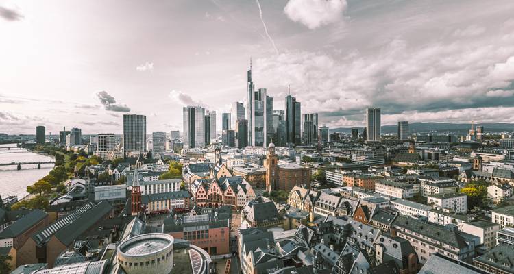 Moderne Skyline von Frankfurt mit emporragenden Glaswolkenkratzern unter dramatischen Wolken, betrachtet von oberhalb des Mains.