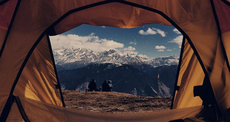 View through tent opening to two campers sitting atop ridge overlooking expansive snowy mountain range