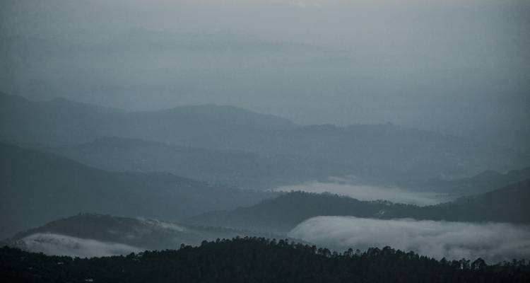 Layers of misty forested hills fading into grey twilight creating a tranquil mood