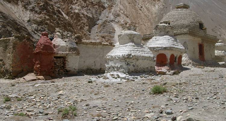 Eine Reihe alter weißgetünchter Chorten und roter Stupas in einer kargen Berglandschaft.
