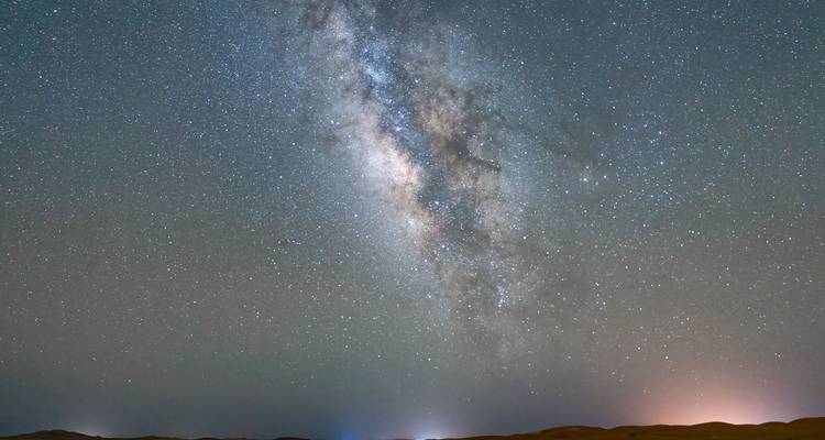 Brillante Voie lactée qui s'étend à travers un ciel désertique dégagé au-dessus de silhouettes de dunes lointaines.