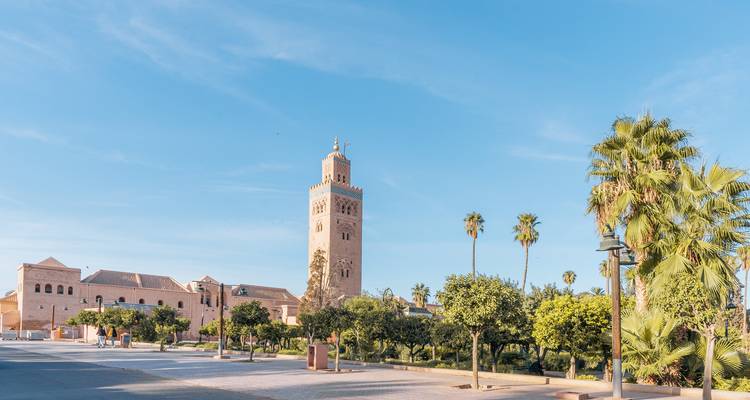 La mosquée Koutoubia et son minaret s'élèvent au-dessus de l'avenue bordée de palmiers sous le ciel bleu limpide de Marrakech.