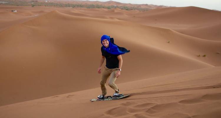 Homme portant un foulard bleu faisant du surf sur sable sur les pentes douces du désert.