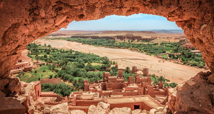 Vue à travers une fenêtre naturelle de roche sur le ksar en adobe et l'oasis verdoyante de la vallée d'Aït Benhaddou
