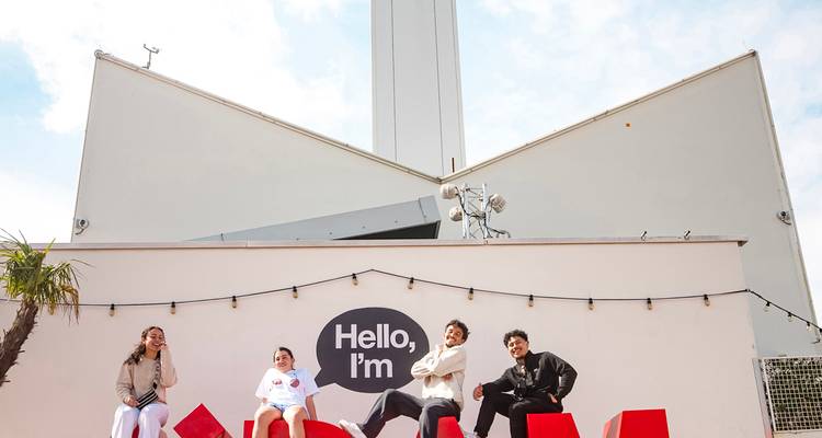 Four friends pose on oversized red letters outside a modern tower that resembles Berlin’s TV Tower.