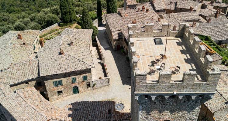 Aerial view of a stone castle tower and medieval village rooftops in rural Tuscany