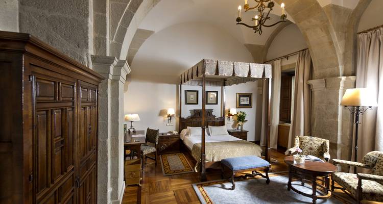 Habitación de hotel histórico con arcos de piedra, cama con dosel y muebles de época de madera.