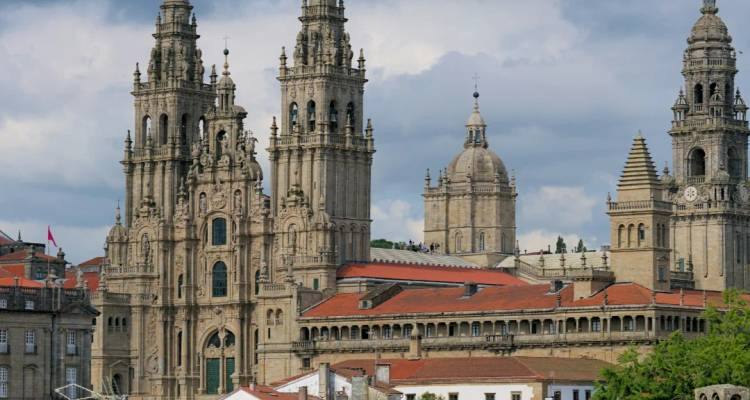 Las torres y agujas barrocas de la Catedral de Santiago de Compostela elevándose sobre techos de tejas rojas bajo un cielo nublado.