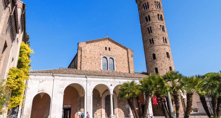 Aus Ziegeln erbaute Basilika mit hohem zylindrischem Glockenturm und Palmen unter klarem blauen Himmel in Ravenna.