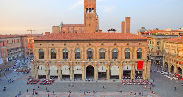 Wijds uitzicht over Bologna's hoofdplein met historische hal en verspreide bezoekers in warm avondlicht.