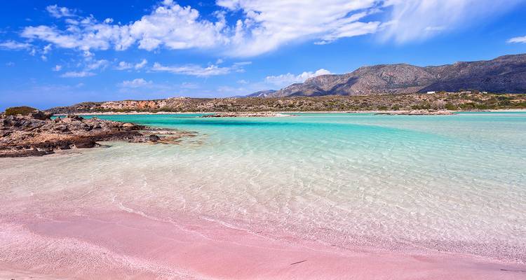 Flache rosafarbene Gewässer und weicher Sand des Elafonissi-Strandes mit türkisfarbenem Meer dahinter.