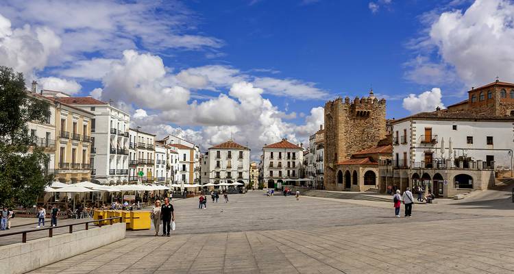 Weiter mittelalterlicher Platz in Cáceres mit historischem Turm, Cafés und vereinzelten Touristen unter einem dramatischen Himmel
