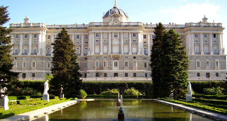 Fachada frontal del Palacio Real de Madrid enmarcada por jardines cuidados y fuentes