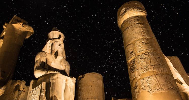 Cielo nocturno lleno de estrellas sobre estatuas y columnas iluminadas dentro del Templo de Luxor.
