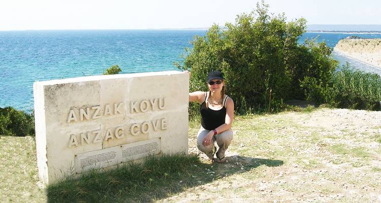Traveler posing beside the ANZAC Cove stone sign overlooking turquoise coastal waters.