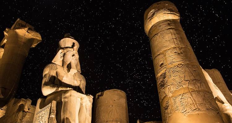 Illuminated statues and columns of Luxor Temple under a star-filled night sky.