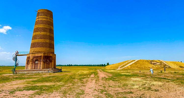 Ancienne tour de briques de Burana s'élevant au-dessus d'une prairie plate avec des visiteurs à proximité.