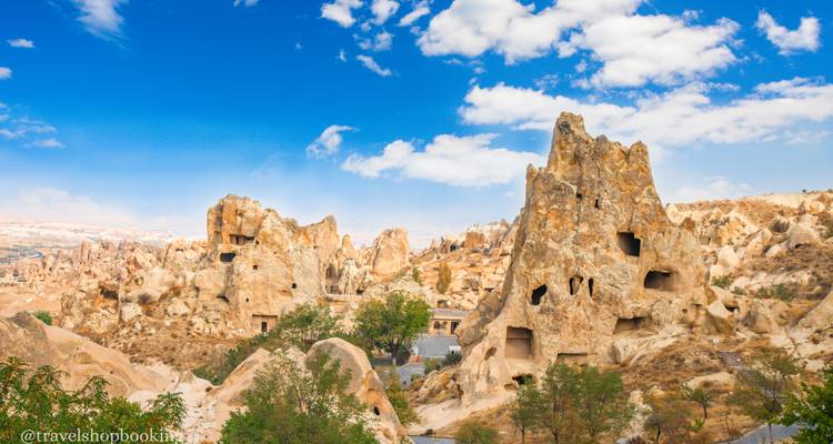 Formaciones rocosas dentadas de chimeneas de hadas perforan un cielo azul brillante salpicado de nubes en Capadocia.