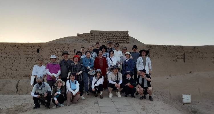 Gran grupo turístico de pie frente a ruinas antiguas de ladrillos de barro al atardecer