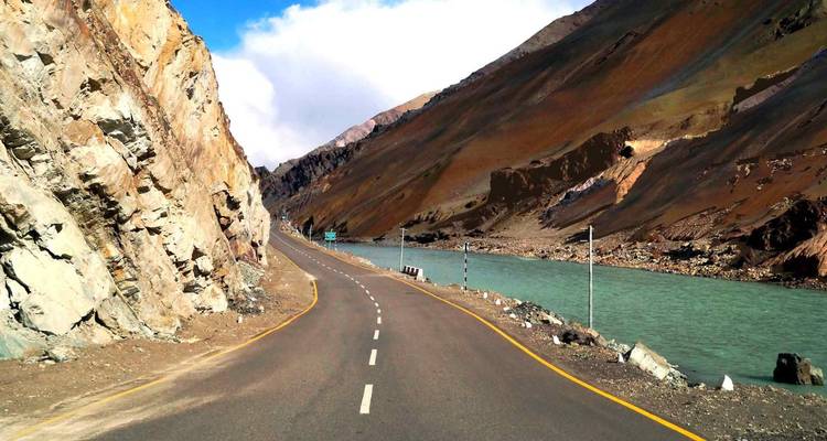 Leere Bergautobahn, die sich neben einem milchig-türkisfarbenen Fluss windet, mit kahlen Hängen, die auf beiden Seiten steil ansteigen.