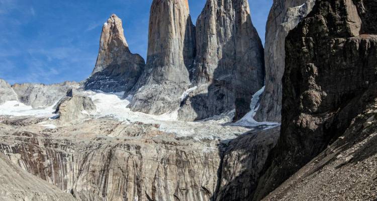 De purs pics de granit s'élevant au-dessus d'une vallée rocheuse avec des plaques de neige persistantes sous un ciel bleu.