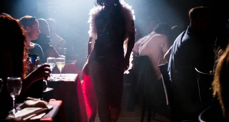 Un spectacle de tango ou de cabaret faiblement éclairé avec un artiste se déplaçant entre les tables des spectateurs illuminées par des chandelles.