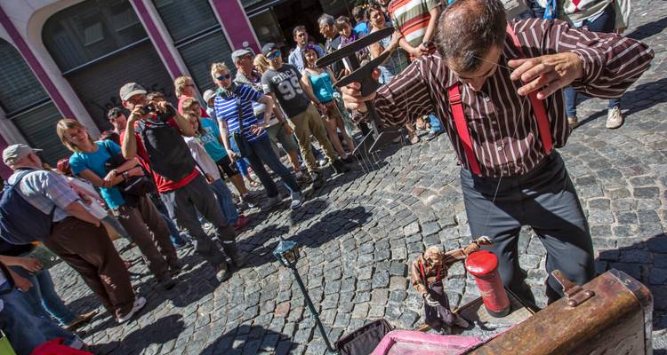 Artiste de rue manipulant une marionnette devant une foule rassemblée sur des rues pavées.