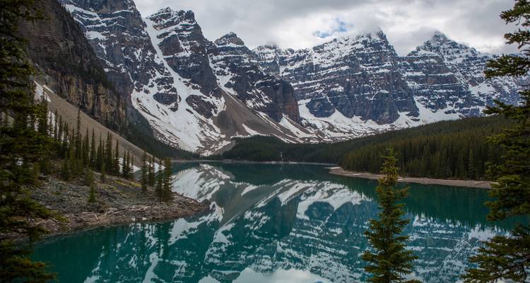Los picos cubiertos de nieve se alzan sobre el lago Moraine de aguas turquesas con reflejos perfectos como en un espejo.